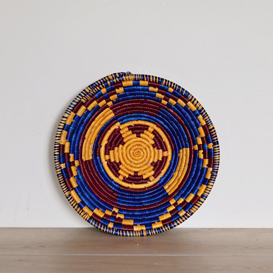 Handwoven Indigo Mosaic Bukedo and Raffia bowl handmade in Uganda featuring deep indigo, golden ochre, and burgundy woven patterns for fair trade home décor.