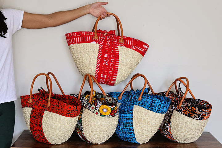 Assorted Kikapu Janet Tote Bags handmade in Kenya from woven palm leaf and colorful African fabric with wooden and leather handles.