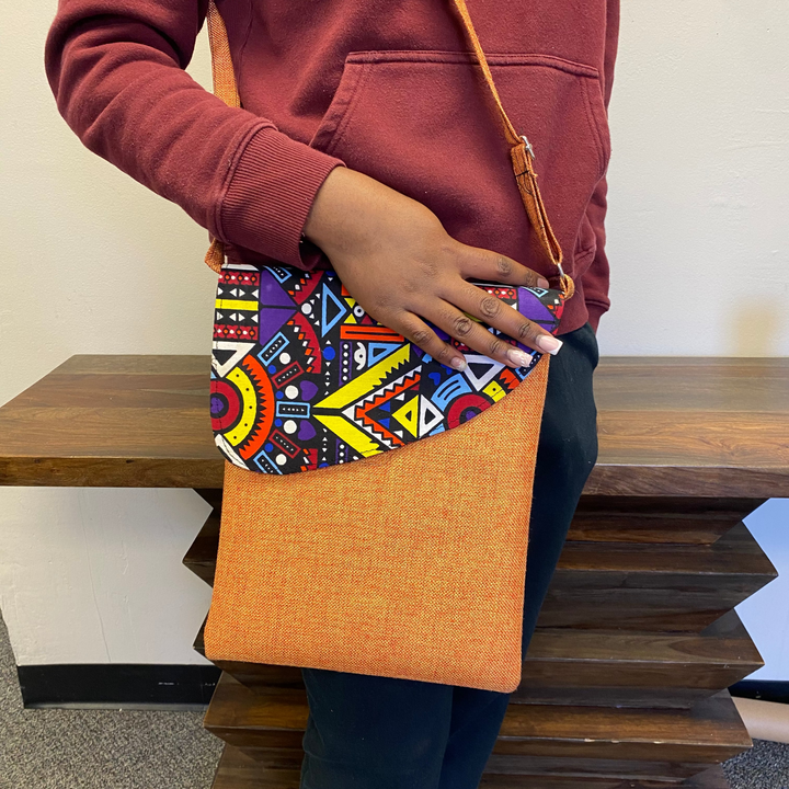 Person holding a colorful, Africa, patterned crossbody bag with an orange base.