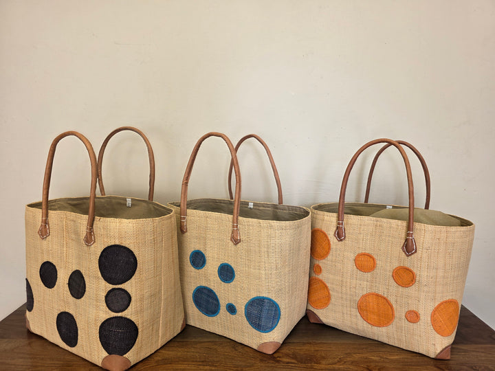 Abstract raffia handbags in orange, black, and teal with leather handles, handwoven in Madagascar by fair trade artisan partners.