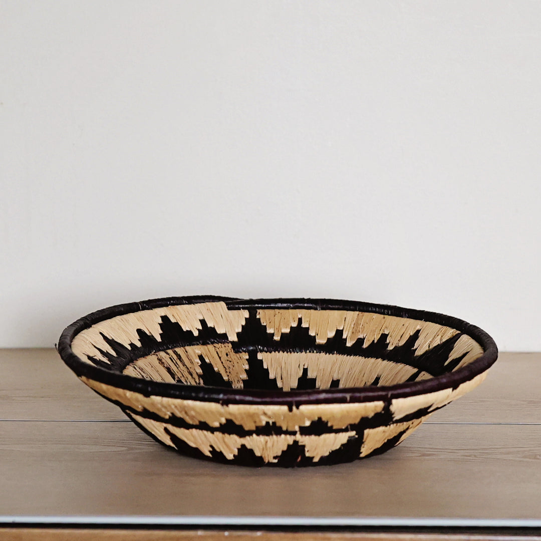 Side view of a Midnight Sun Bukedo and Raffia bowl handcrafted in Uganda from banana leaf stalks and palm raffia with dramatic black and natural woven details.