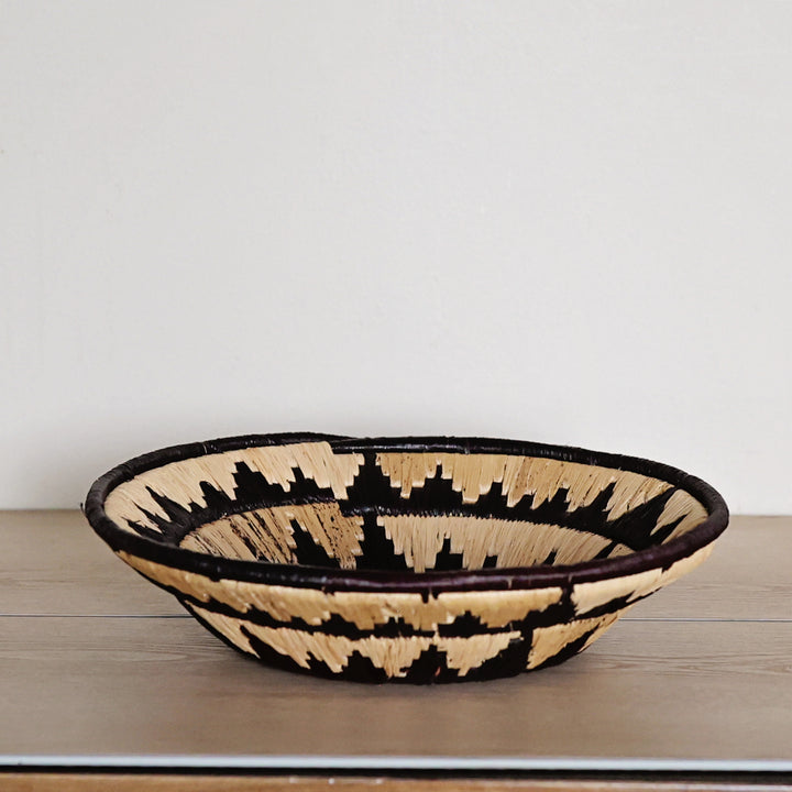 Side view of a Midnight Sun Bukedo and Raffia bowl handcrafted in Uganda from banana leaf stalks and palm raffia with dramatic black and natural woven details.