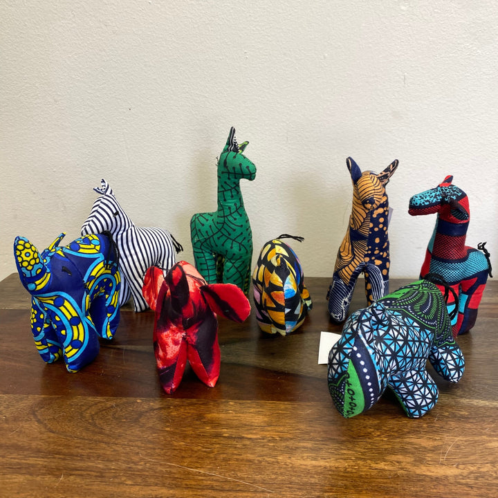 Colorful, fair-trade stuffed animal toys on a wooden surface with a plain background.