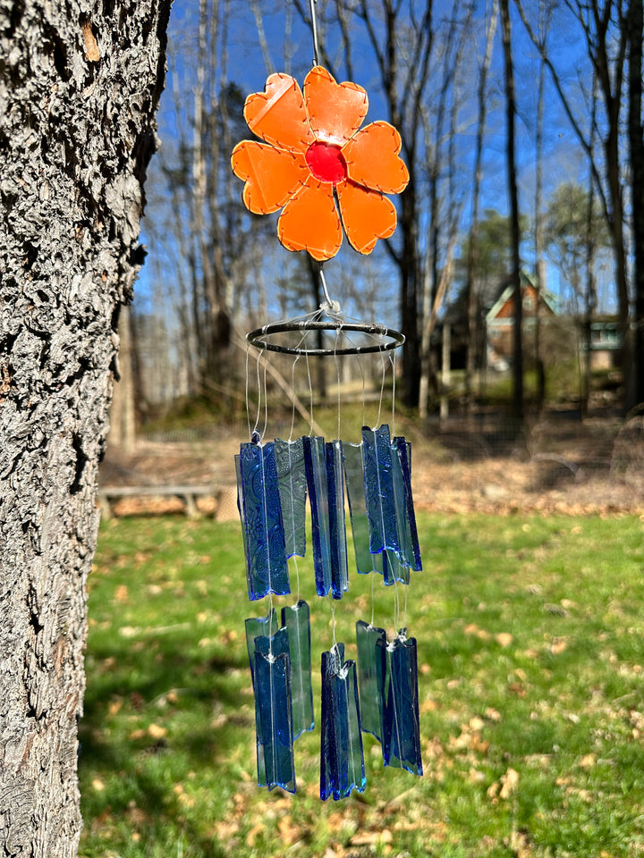 Decorative glass flower with orange center and blue petals hanging from a tree branch.