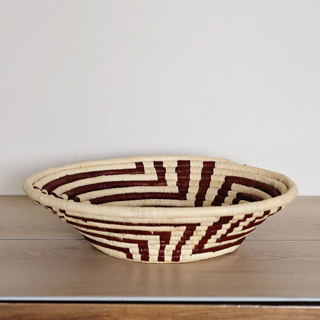 Side view of a Radiant Weave Bukedo and Raffia bowl handcrafted in Uganda from banana leaf stalks and palm raffia in rich burgundy and natural tones.