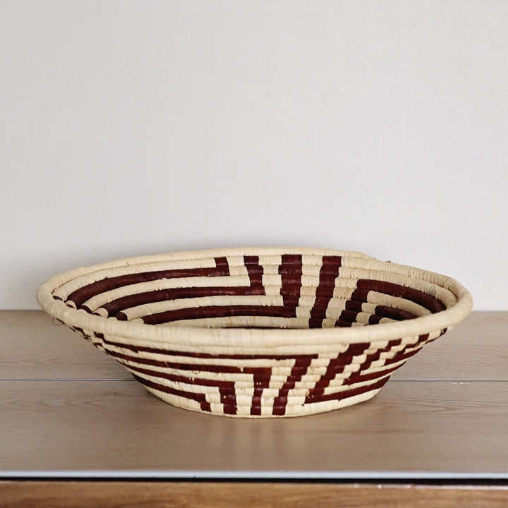 Side view of a Radiant Weave Bukedo and Raffia bowl handcrafted in Uganda from banana leaf stalks and palm raffia in rich burgundy and natural tones.