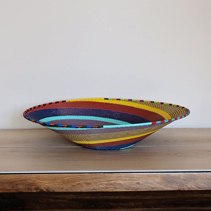 Side view of a Rainbow Zulu Large Shallow Basket featuring colorful handwoven wire craftsmanship by South African artisans.