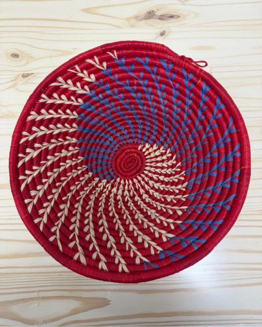 Close-up of intricate red and blue spiral patterns handwoven from natural raffia.