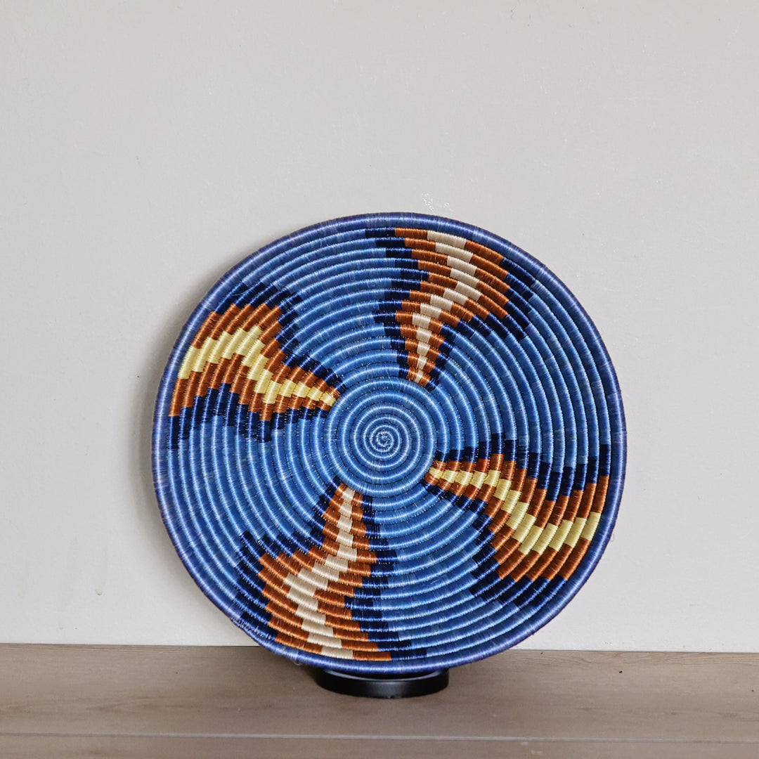 Handwoven Rwanda sisal basket in blue, red, and white geometric patterns viewed from above for fair trade wall décor.
