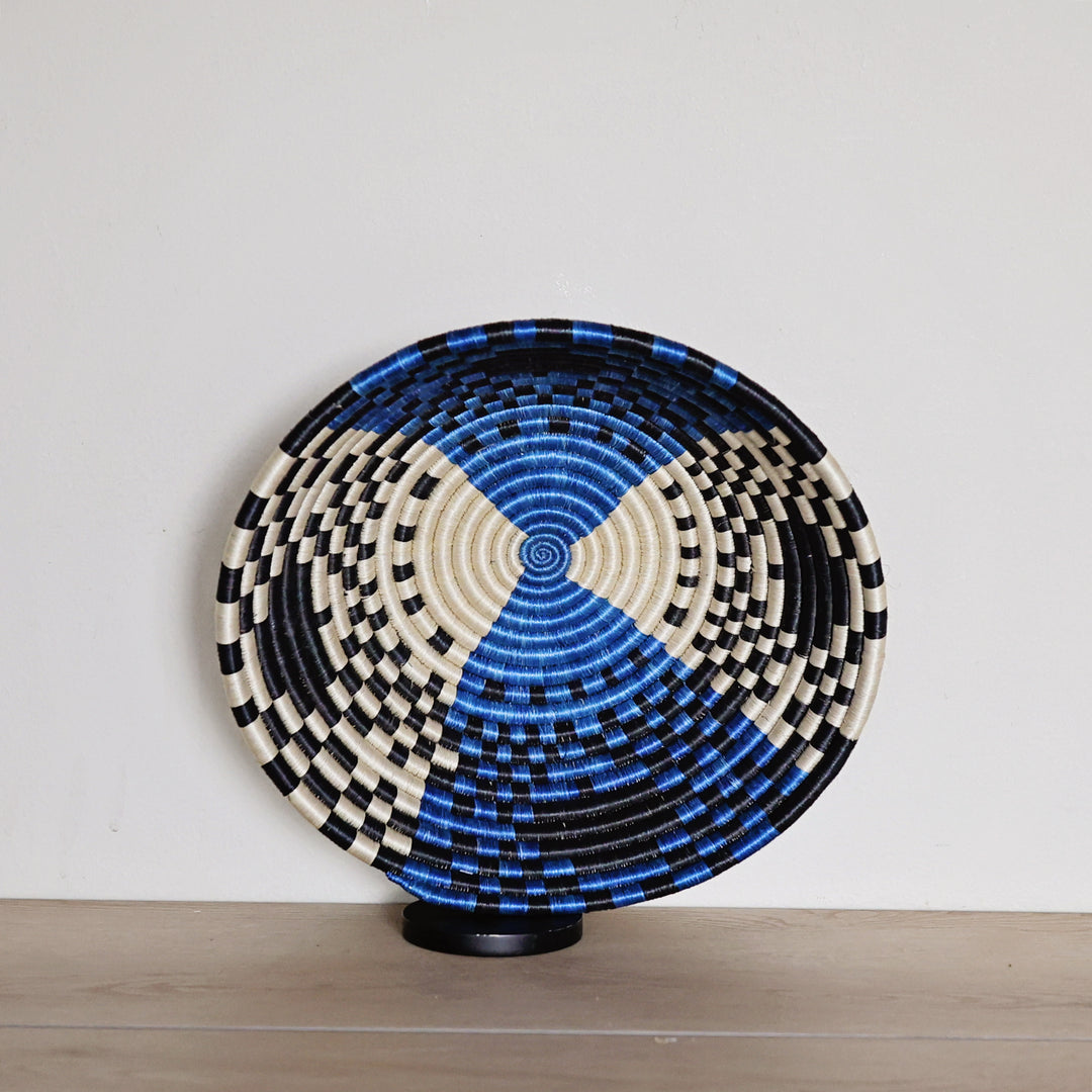 Handwoven Rwanda sisal basket in bright blue, black, and white geometric patterns viewed from above for fair trade wall décor.