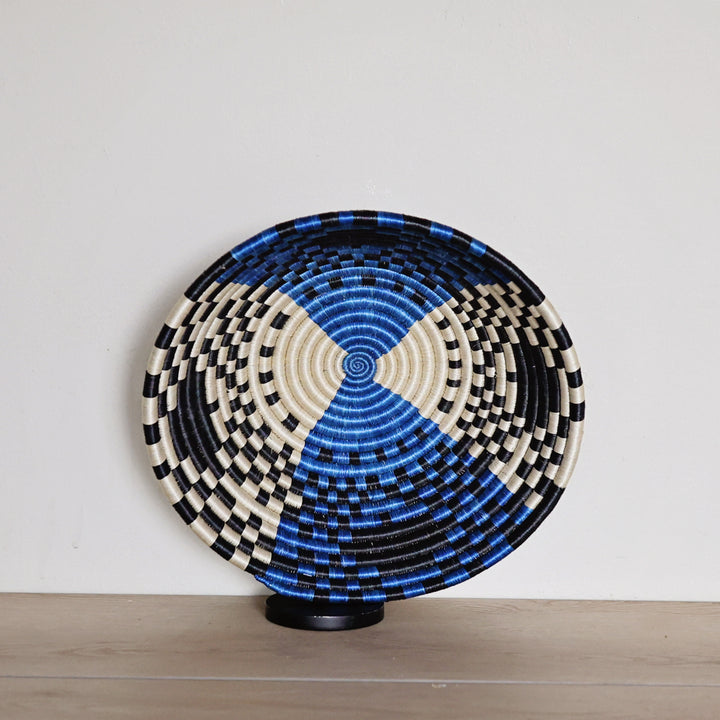 Handwoven Rwanda sisal basket in bright blue, black, and white geometric patterns viewed from above for fair trade wall décor.