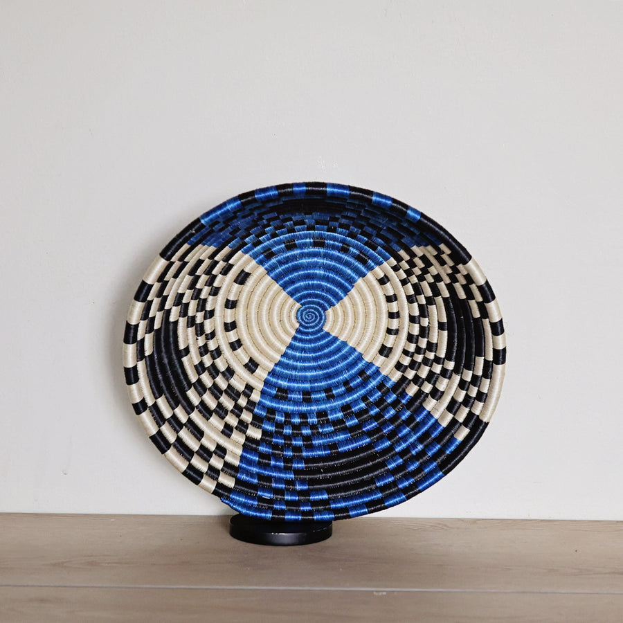 Handwoven Rwanda sisal basket in bright blue, black, and white geometric patterns viewed from above for fair trade wall décor.