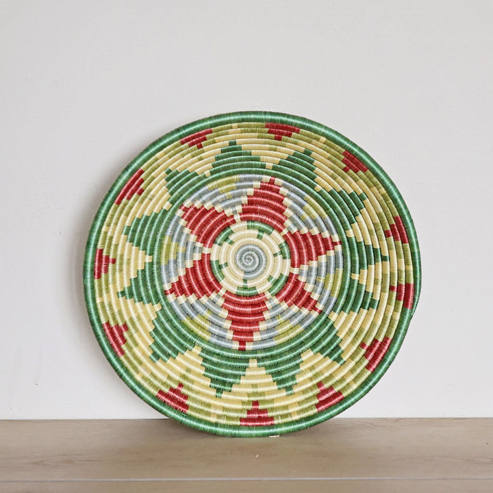 Handwoven Rwanda sisal basket in green, light blue, and red geometric patterns viewed from above for fair trade wall décor.