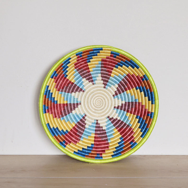 Handwoven Rwanda sisal basket featuring a vibrant multicolor spiral pattern viewed from above for fair trade wall décor.