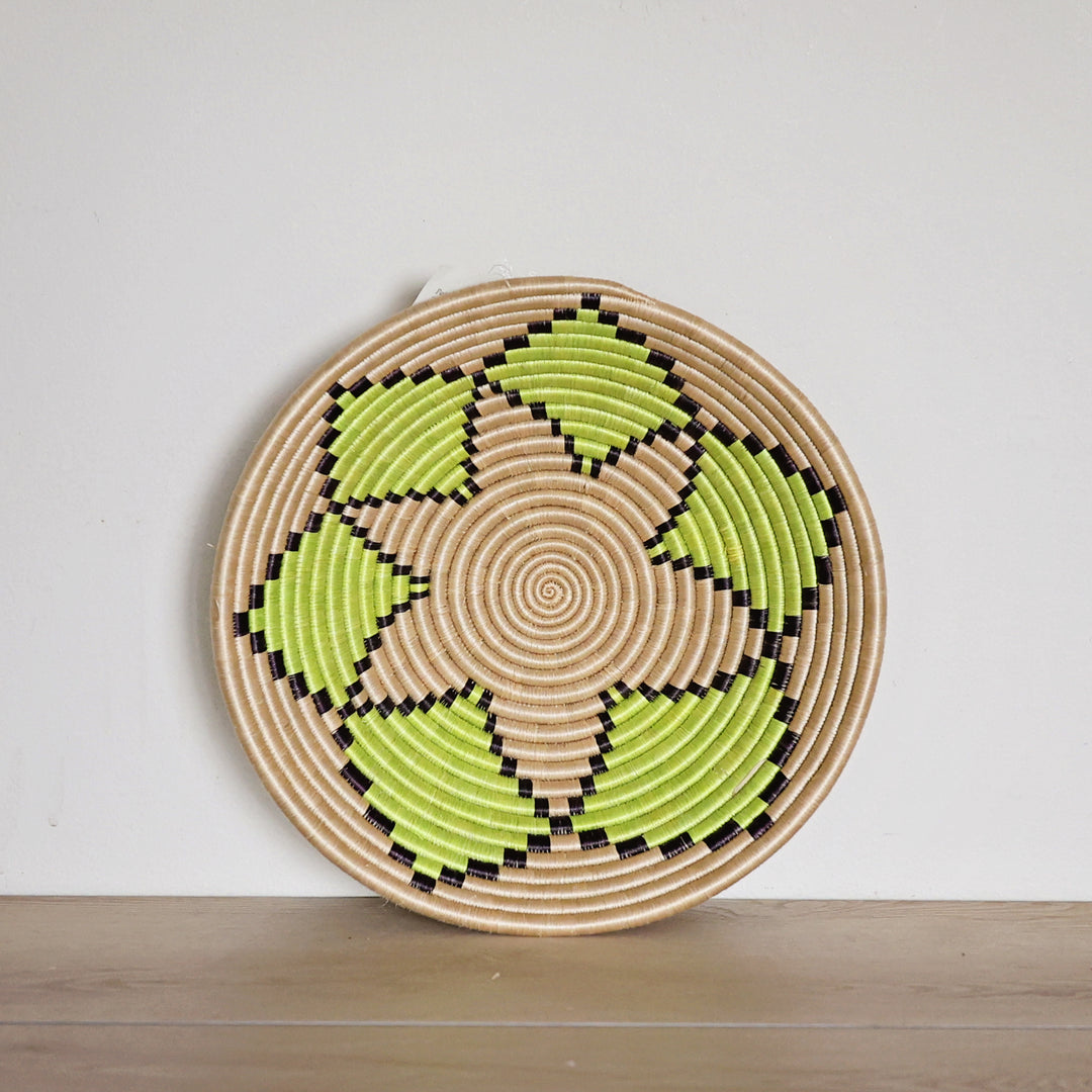 Handwoven Rwanda sisal basket with a natural background and green floral pattern viewed from above for fair trade wall décor.