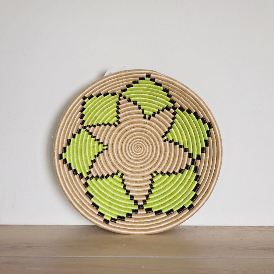 Handwoven Rwanda sisal basket with a natural background and green floral pattern viewed from above for fair trade wall décor.