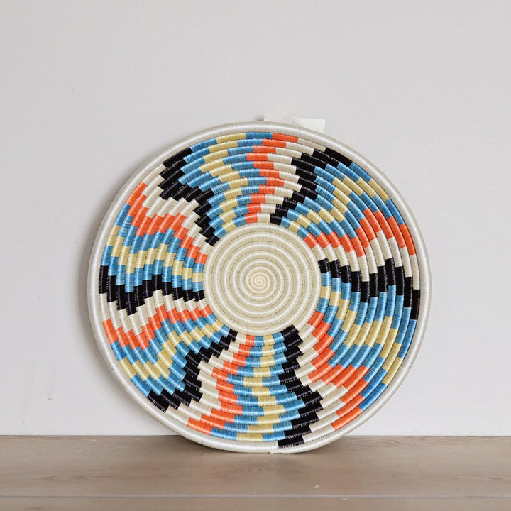 Handwoven Rwanda sisal basket in white with multicolored geometric patterns viewed from above for fair trade wall décor.