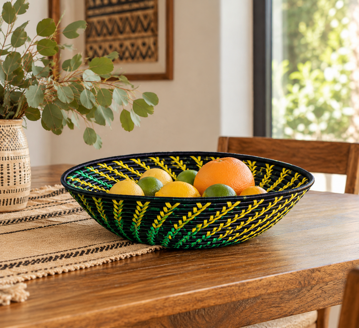 Yellow, green and black handwoven raffia fruit basket displayed with citrus fruit on a dining table.