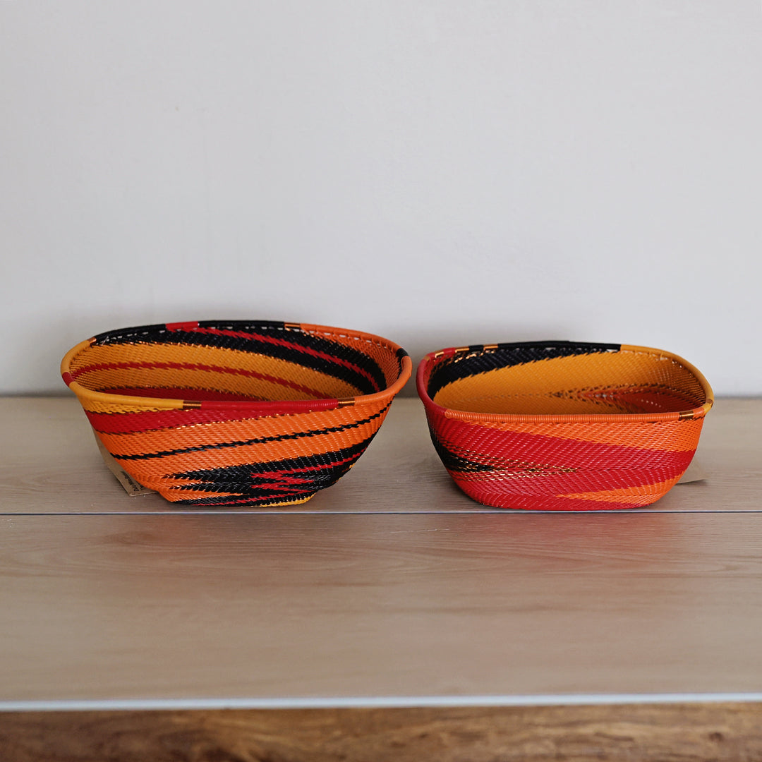 Round Sunset Zulu large square bowl basket featuring a handwoven red, orange, yellow and black spiral pattern.