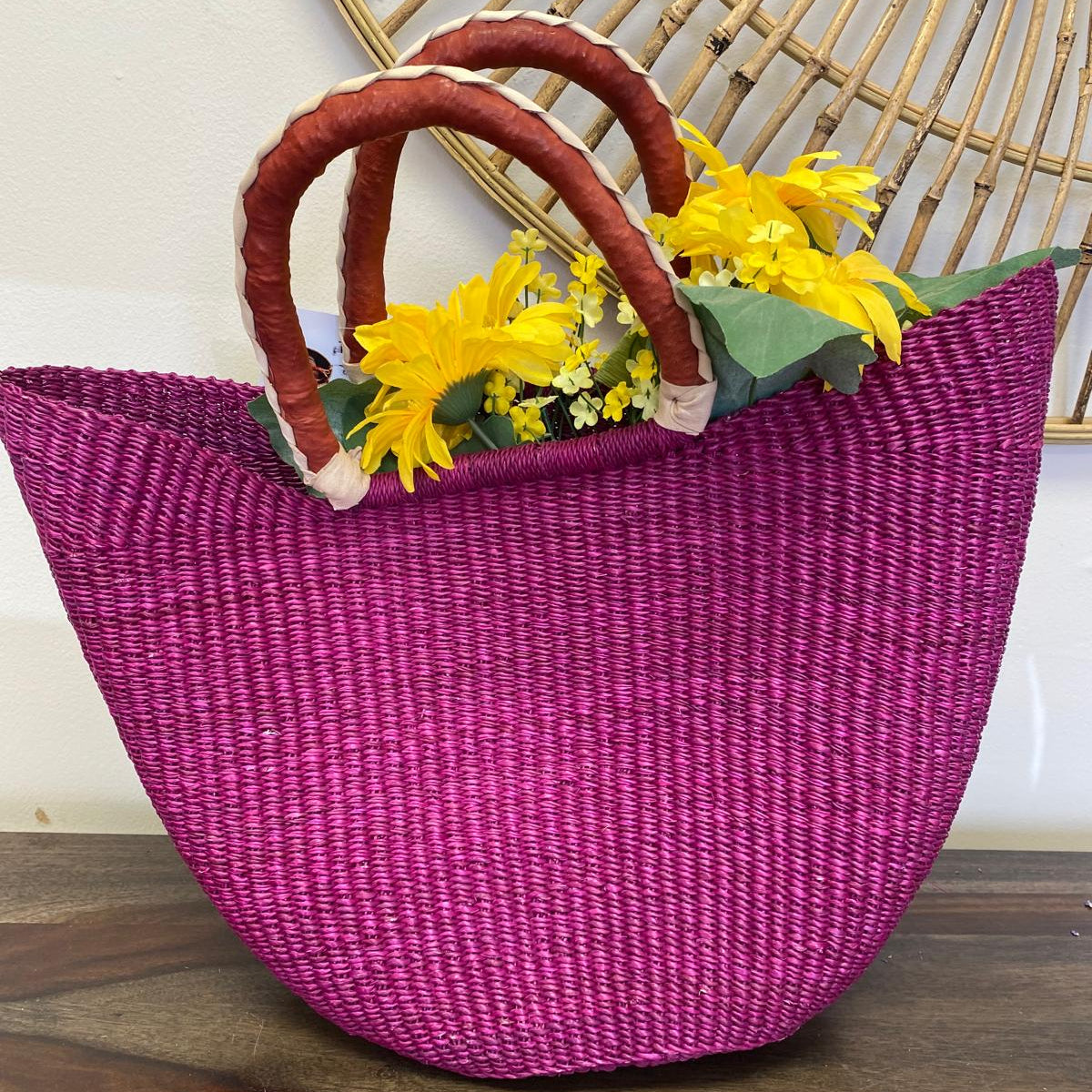 Pink, fair-trade, woven bag with red handles and yellow flowers on a wooden surface.