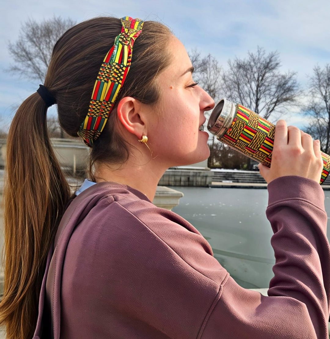 Person drinking from an African printed insulated water bottle outside. 