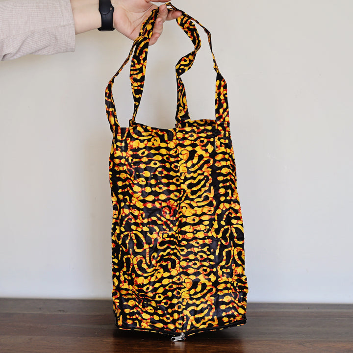 Yellow and black tote bag with a batik print pattern held by a person against a plain background.