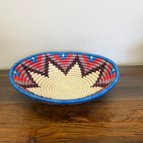 Handwoven Zigzag Peaks Rwanda sisal basket with blue, red, brown, and natural geometric patterns viewed from above.