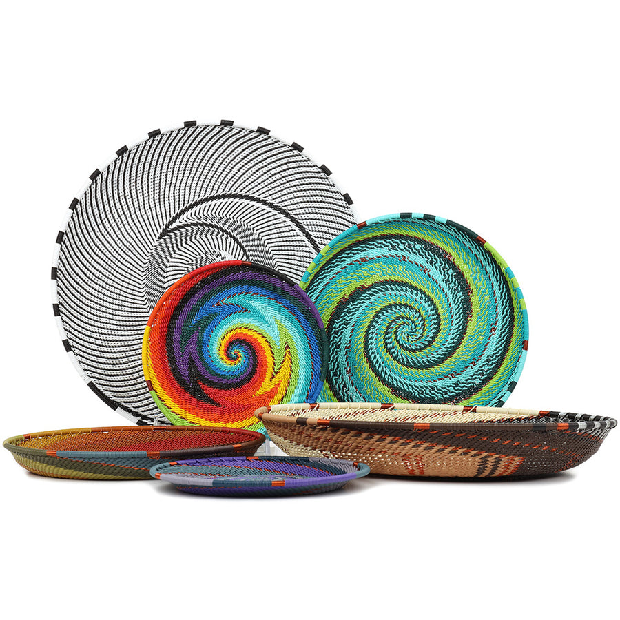 A set of six hand-woven Zulu decorative trays with vibrant, intricate spiral and geometric patterns in black, white, blue, green, red, orange, yellow, and brown, arranged on a clean white background.